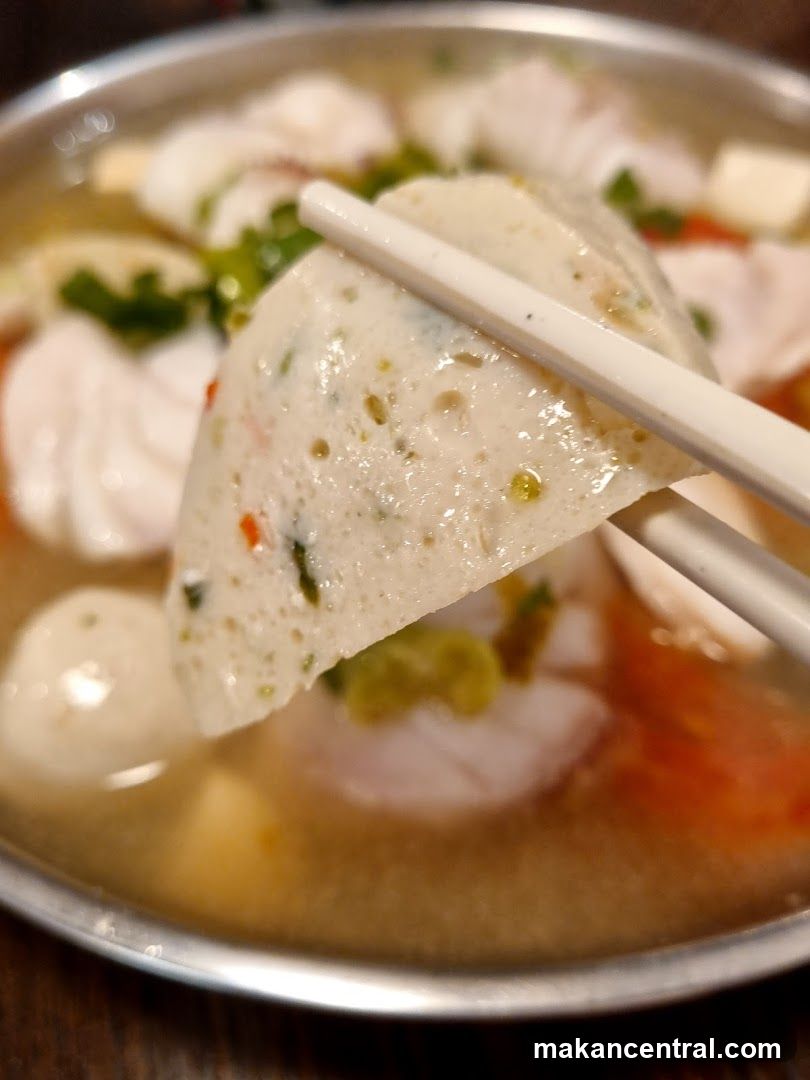 Close-up of a piece of fish cake being held by chopsticks over a bowl of soup.