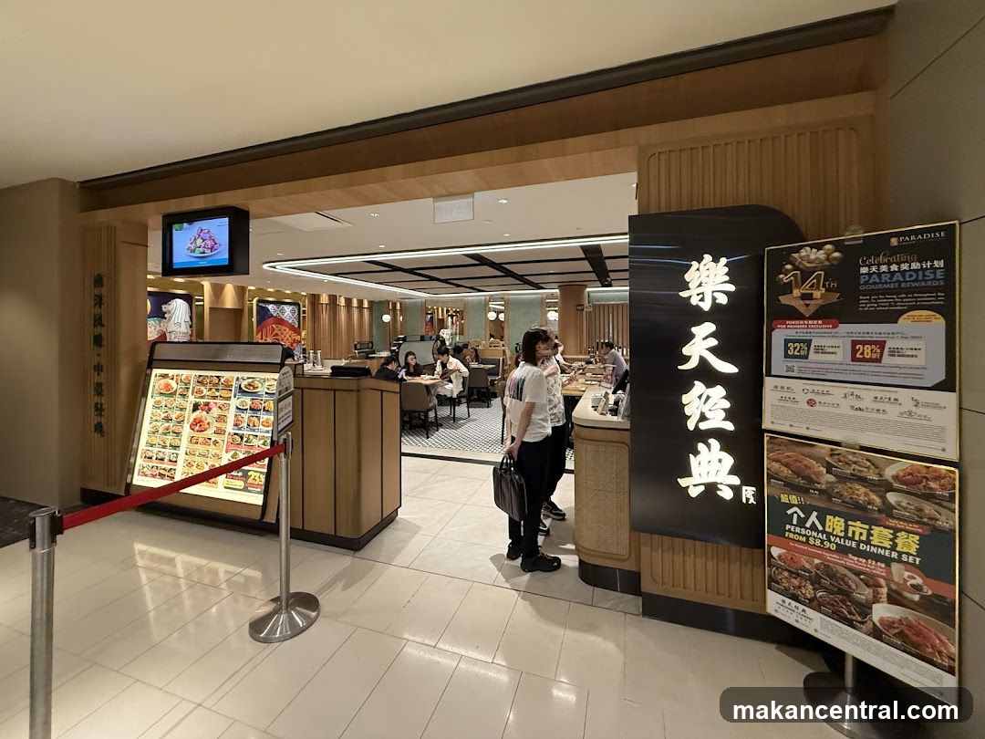The exterior entrance of a restaurant with a large sign displaying Chinese characters and promotional posters. A menu board is displayed to the left, and the interior of the restaurant is visible through the entrance.