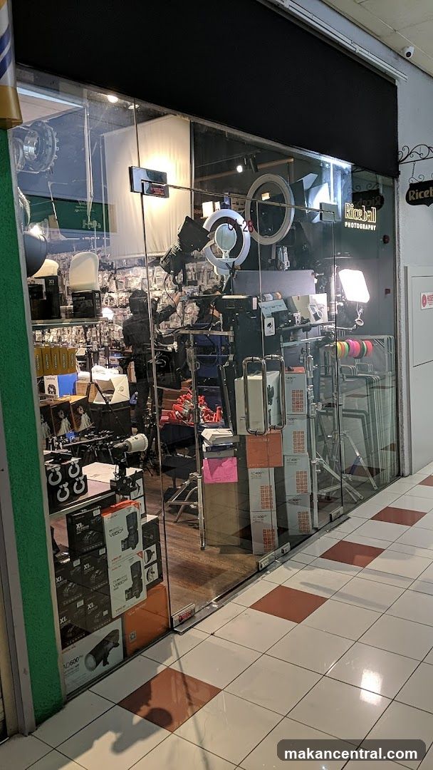 A storefront for Riceball Photography, showcasing a variety of photography equipment through its glass facade. The interior is filled with lighting equipment, cameras, tripods, and boxes of gear.