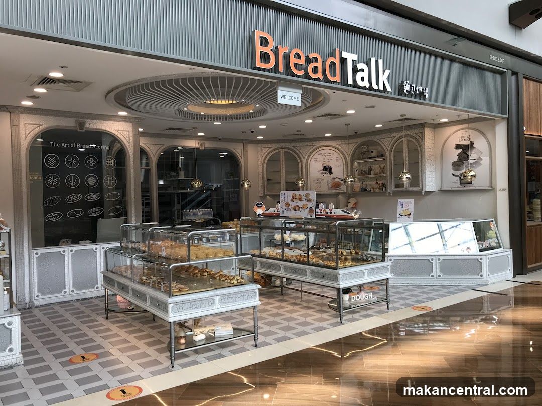The exterior of a BreadTalk bakery. Display cases filled with bread and pastries are visible inside. The shop has a modern design with decorative elements and signage.