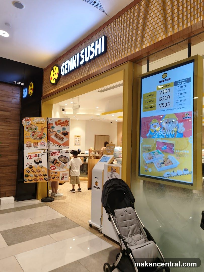 The exterior of a Genki Sushi restaurant with its prominent signage. A digital display shows current queue numbers and estimated wait times for different party sizes. To the left, promotional posters display sushi items and a lunch special. A stroller is parked in front of the entrance.