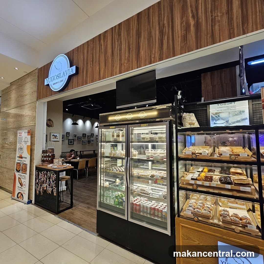 The exterior of Yugoslavia Bakery & Cafe, showing its entrance, display cases filled with pastries and drinks, and seating area inside.