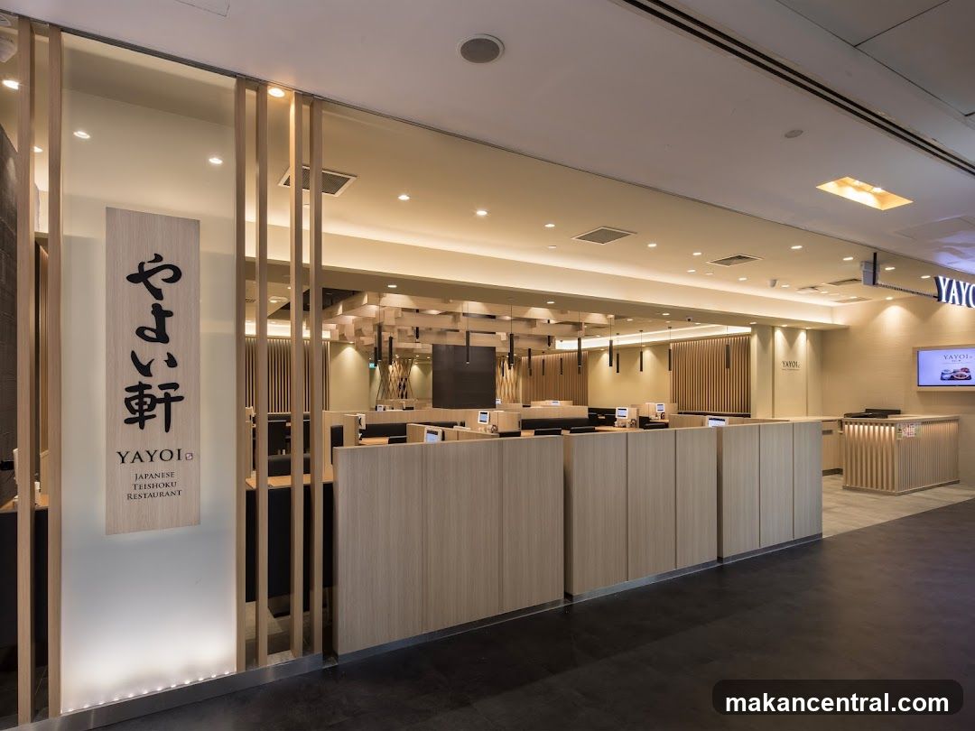 The exterior of a Japanese restaurant called Yayoi. A vertical sign with Japanese characters and the text "YAYOI JAPANESE TEISHOKU RESTAURANT" is visible on the left side of the entrance. The interior of the restaurant, with wooden partitions and tables, is visible through the open entrance.