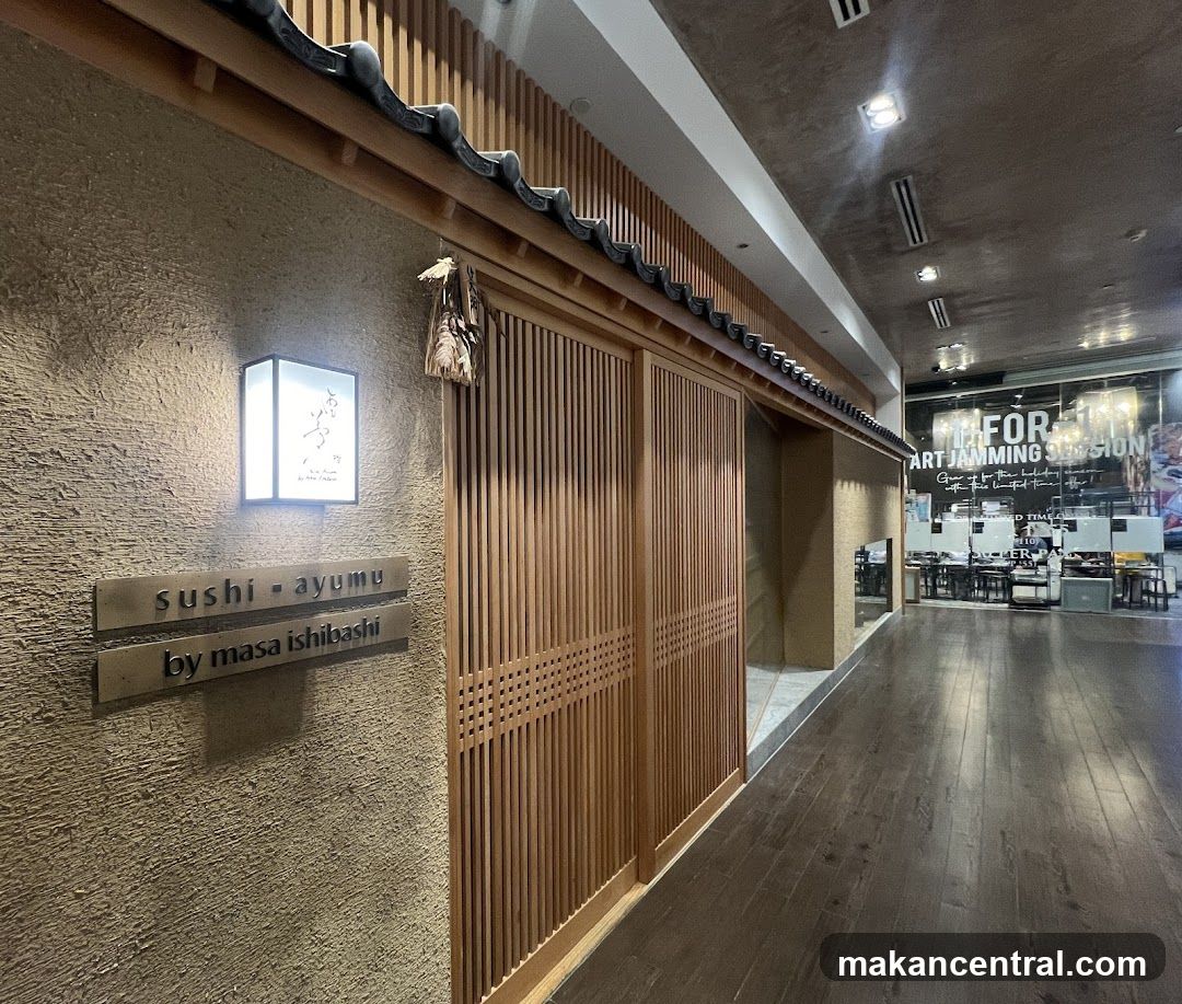 The exterior of a Japanese restaurant with traditional wooden sliding doors and a textured wall. A lit sign displays the restaurant's name and the chef's name.