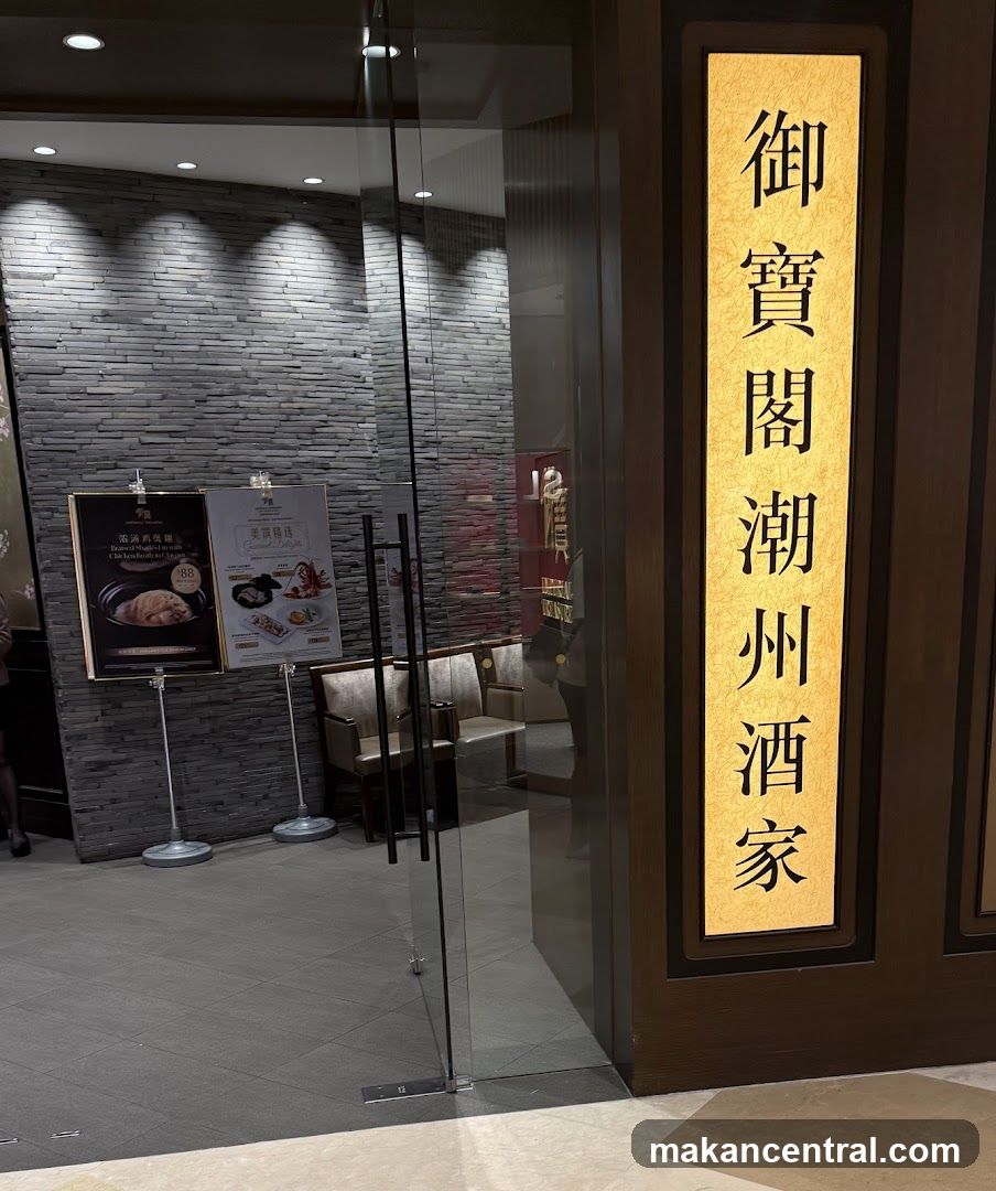 A vertical golden sign with Chinese characters is illuminated on a dark wooden panel next to a glass door. Inside, two display boards show food items and prices.