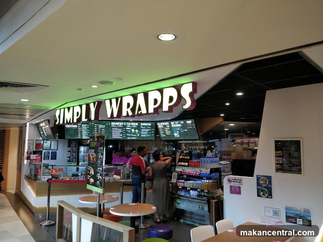 The exterior of a food establishment with a prominent "SIMPLY WRAPPS" sign. The counter area displays various food items and beverages. Several menus are visible, along with seating areas.