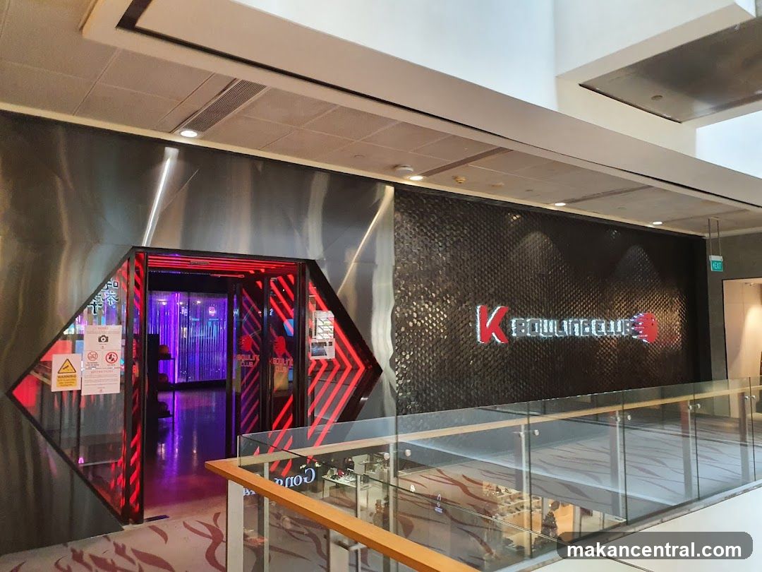 The entrance to K Bowling Club features a striking facade with a diamond-shaped opening framed by red neon lights. The club's name,