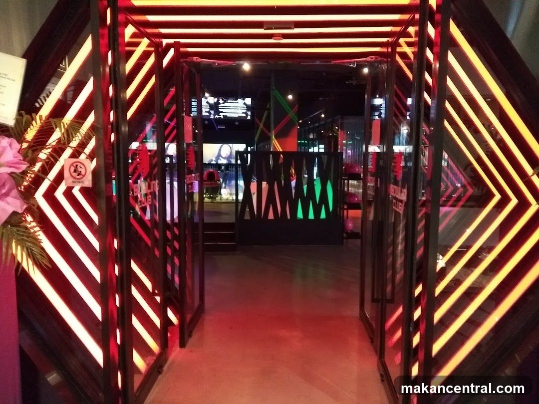 The entrance to a bowling club is illuminated with vibrant red and yellow neon lights arranged in a chevron pattern. The double glass doors are open, revealing the interior which features more neon lighting and what appears to be a bowling alley. A sign with a "No Pets" symbol is visible on the left side of the entrance.