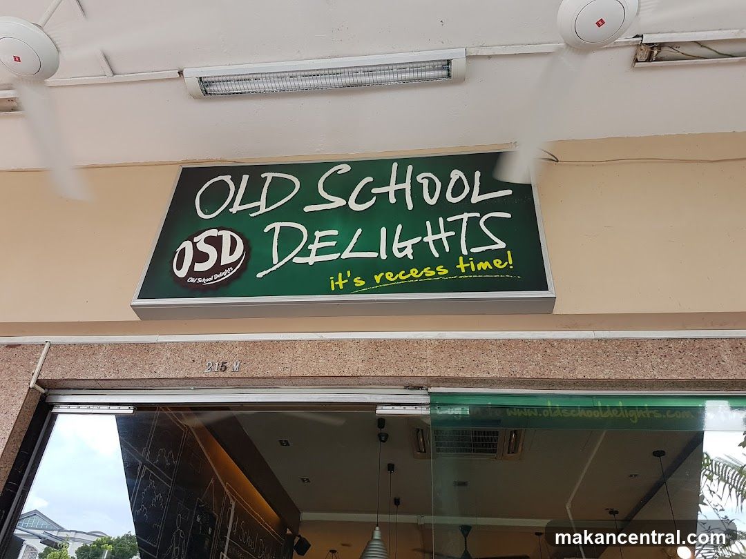 A sign above a storefront reads "OLD SCHOOL DELIGHTS OSD it's recess time!". The sign is green with white and yellow lettering. Below the sign is a glass storefront with a reflection of the interior. A website address, "www.oldschooldelights.com", is visible on the glass.