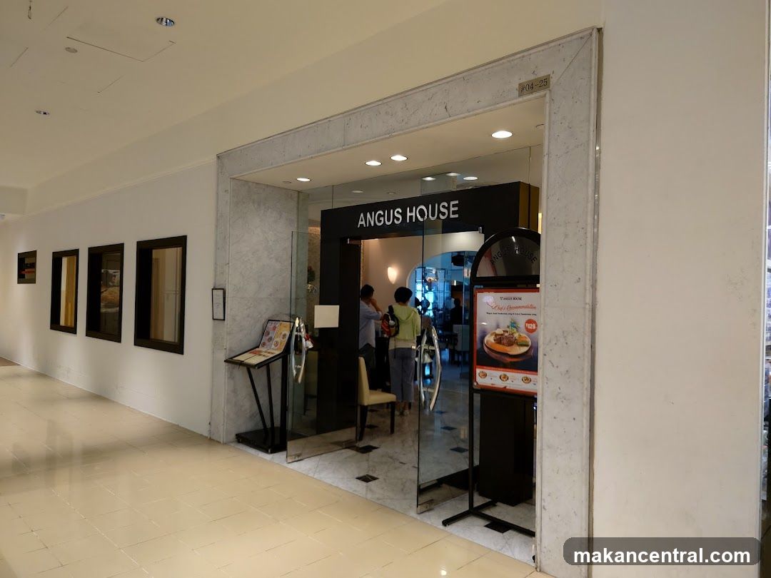The storefront of Angus House is framed by a marble border with the shop name in white lettering on a black sign above the glass entrance. The interior is partially visible through the glass doors, showing patrons inside. A small plaque marked #04-25 is mounted above the entrance frame.