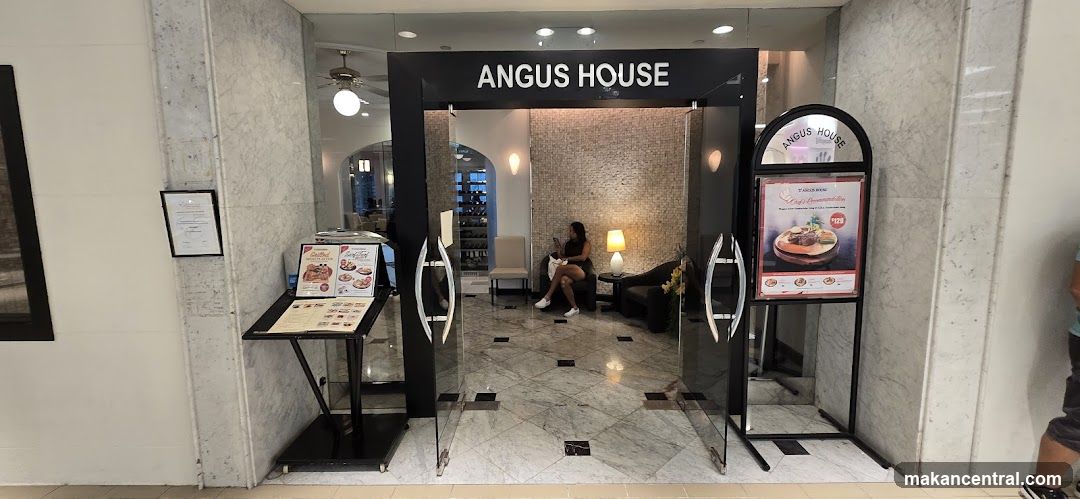 Modern glass doors with black frame, signage 'ANGUS HOUSE' above entrance. Interior features marble flooring, a seated customer, ambient lighting, and a ceiling fan. Marble-clad walls flank the entrance.