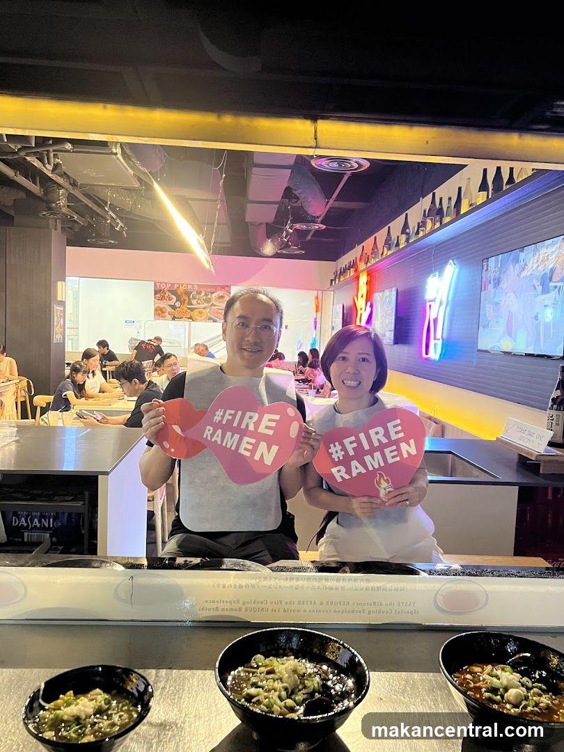 Two people holding #FIRE RAMEN signs at a ramen restaurant