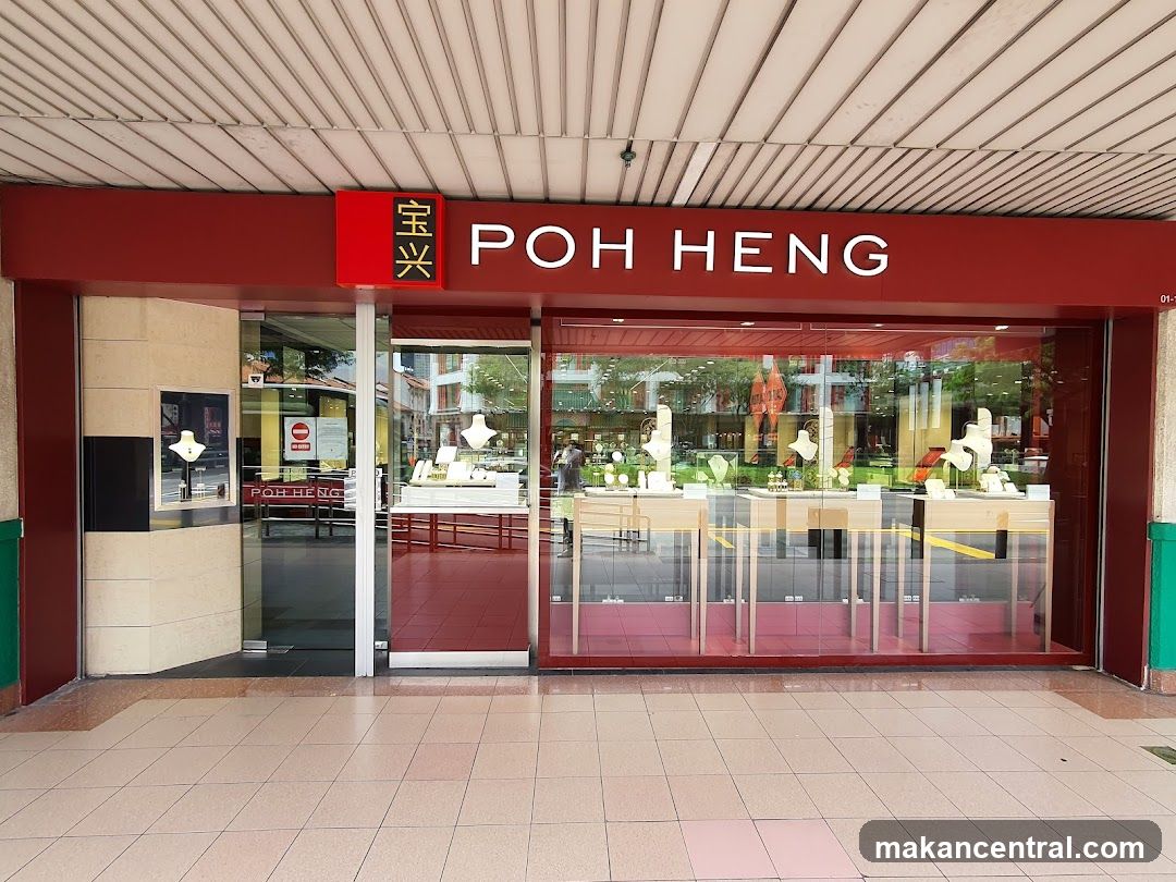 A storefront with a red sign displaying "POH HENG" in white letters and Chinese characters to the left. The entrance has glass doors and windows showcasing jewelry displays inside. The ceiling above is slatted beige, and the floor outside is tiled in light pink and beige tones.