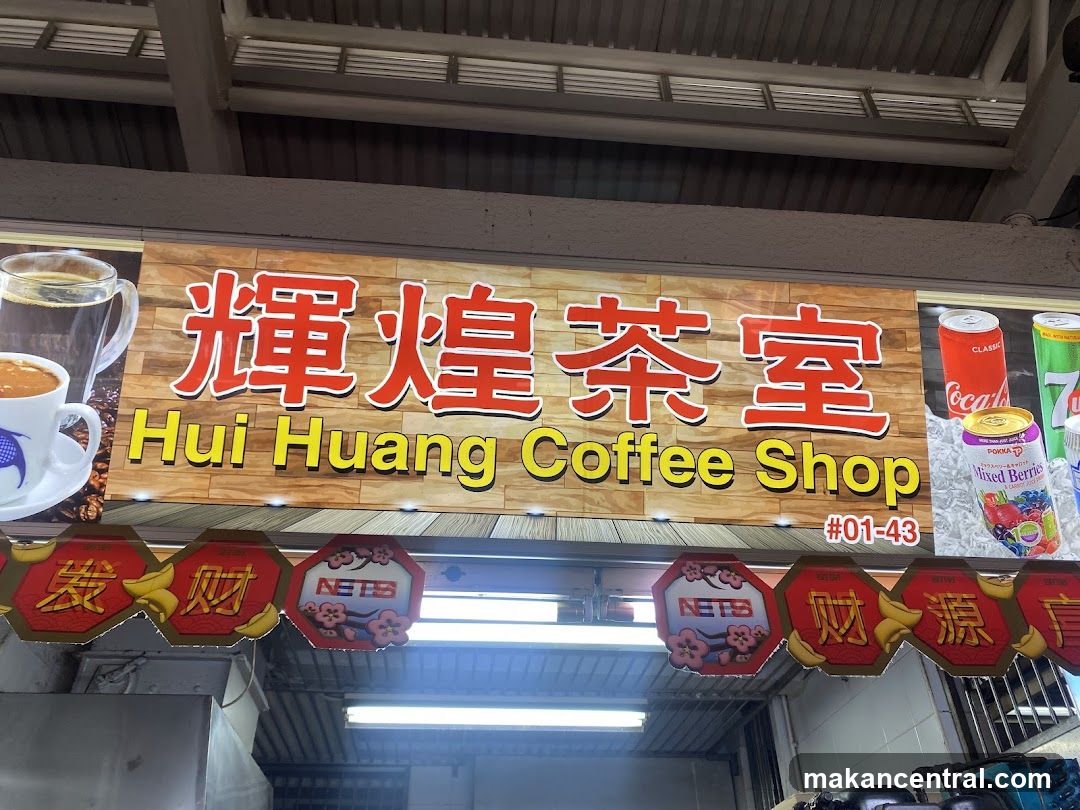 Storefront sign with red Chinese characters "輝煌茶室" and yellow English text "Hui Huang Coffee Shop" on a wooden-textured background. Sign includes unit number #01-43. Below the main sign, decorative red hexagonal signs with gold characters (e.g., "發財", "财源") and "NETS" logos are mounted under fluorescent lighting. The ceiling has metal beams and ventilation slats. No menu or interior visible.