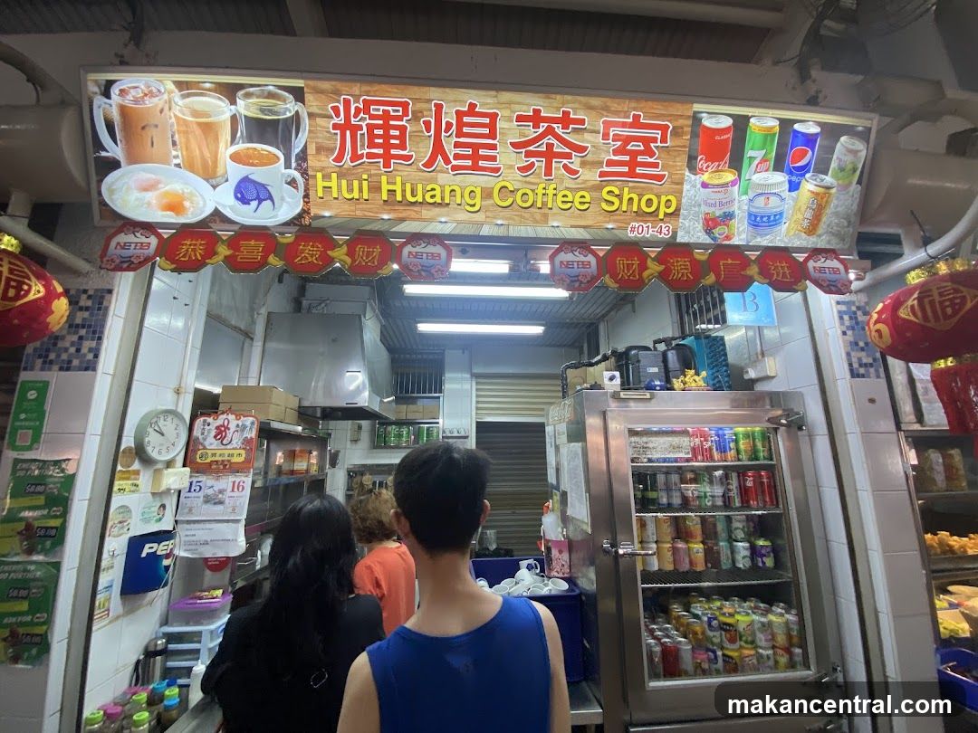 Exterior storefront with signboard displaying "輝煌茶室" and "Hui Huang Coffee Shop #01-43". Above the entrance, a banner shows beverages and soda cans. Red decorative lanterns hang on either side. Inside, customers are seen facing the counter; a refrigerator stocked with canned drinks is to the right.