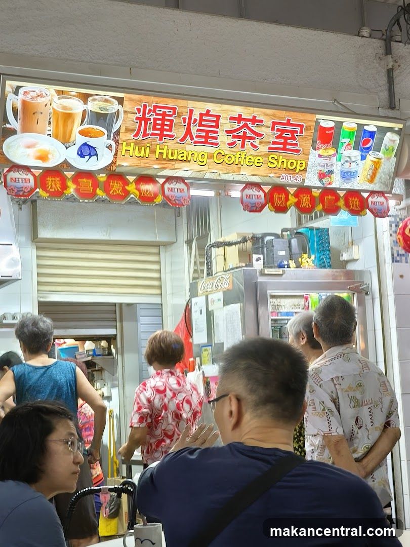 A storefront with a large sign displaying "輝煌茶室" and "Hui Huang Coffee Shop #01-43" in red and yellow lettering. The sign features images of beverages and canned drinks like Coca-Cola, Pepsi, and 7UP. Red decorative lanterns hang below the sign. Customers are seen inside and outside the shop, some facing away from the camera. A refrigerator is visible on the right side of the counter area.