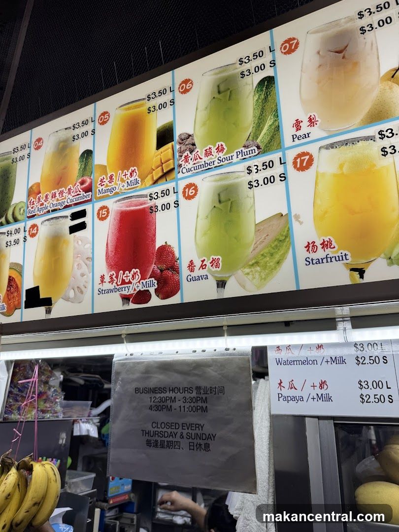 A large printed menu board displaying various fruit smoothies with prices in Singapore dollars. Items include Red Apple Orange Cucumber, Mango + Milk, Strawberry + Milk, Guava, Cucumber Sour Plum, Pear, Starfruit, Watermelon + Milk, and Papaya + Milk. Business hours are listed as 12:30 PM - 3:30 PM and 4:30 PM - 11:00 PM, closed every Thursday & Sunday.