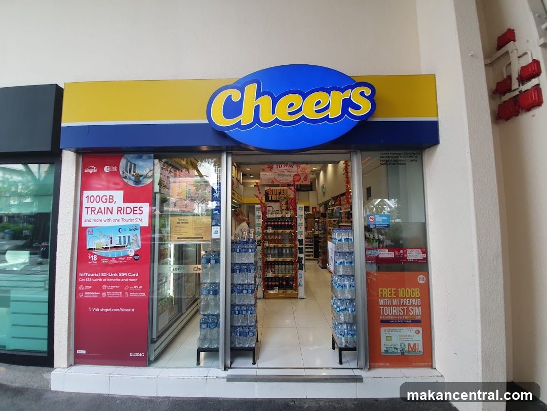 Exterior view of Cheers store entrance with prominent blue and yellow logo above glass doors. Visible interior includes shelves stocked with products, water bottles displayed on stands, and promotional posters on the left and right windows advertising SIM cards and 100GB data offers. The shop appears to be a convenience store or supermarket.