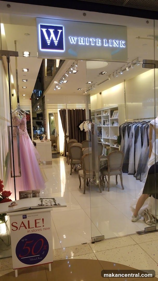 Glass storefront with illuminated 'W WHITE LINK' sign above entrance. Interior visible through glass: display of wedding gowns, seating area, shelving units, and racks of attire. Promotional sale sign on floor outside reads 'SALE! in stores now up to 50% off Selected Items'.