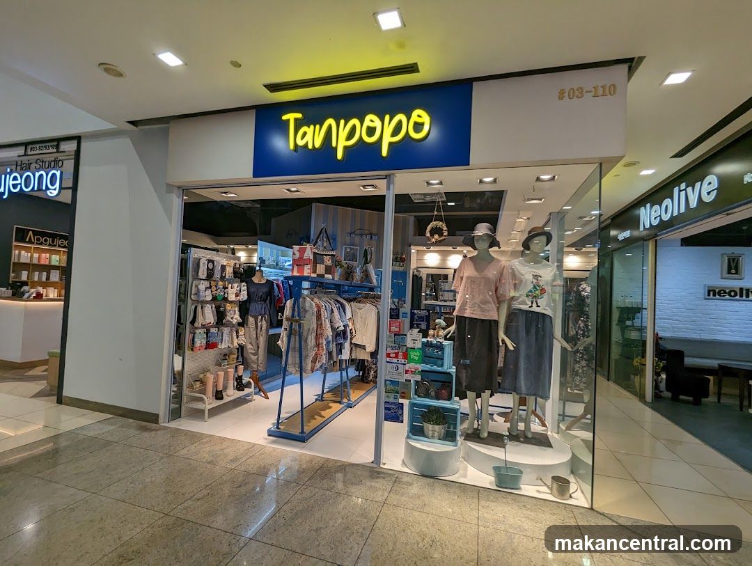 Storefront with illuminated yellow 'Tanpopo' sign on blue background above glass entrance. Display includes mannequins wearing clothing, racks of apparel, and shelves with accessories. Shop number #03-110 is visible in top right corner. Adjacent stores include 'Neolive' to the right and 'Hair Studio' to the left.