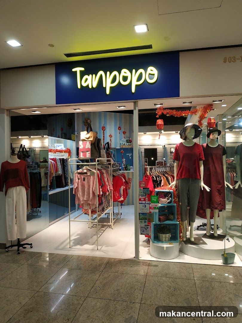 Store entrance with illuminated neon sign reading 'Tanpopo' on a blue background. Display windows feature mannequins dressed in red attire, racks of clothing inside, and festive red decorations including lanterns. The floor is tiled, and the interior lighting is bright. No menu or printed materials are visible.