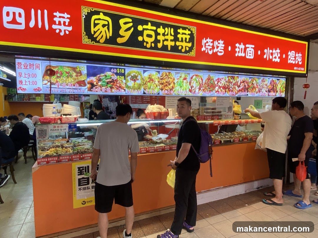 A brightly lit storefront with a red signboard featuring Chinese characters. The sign includes '四川菜' (Sichuan cuisine), '家乡凉拌菜' (homeland cold noodles), and '烧烤·拉面·水饺·馄饨' (grilled meat, noodles, dumplings). Below the main sign is an illuminated menu board displaying food images and prices in Hong Kong dollars. Customers are seen standing at the counter, some holding bags or waiting to order. A yellow EASI sticker is visible on the orange counter wall.