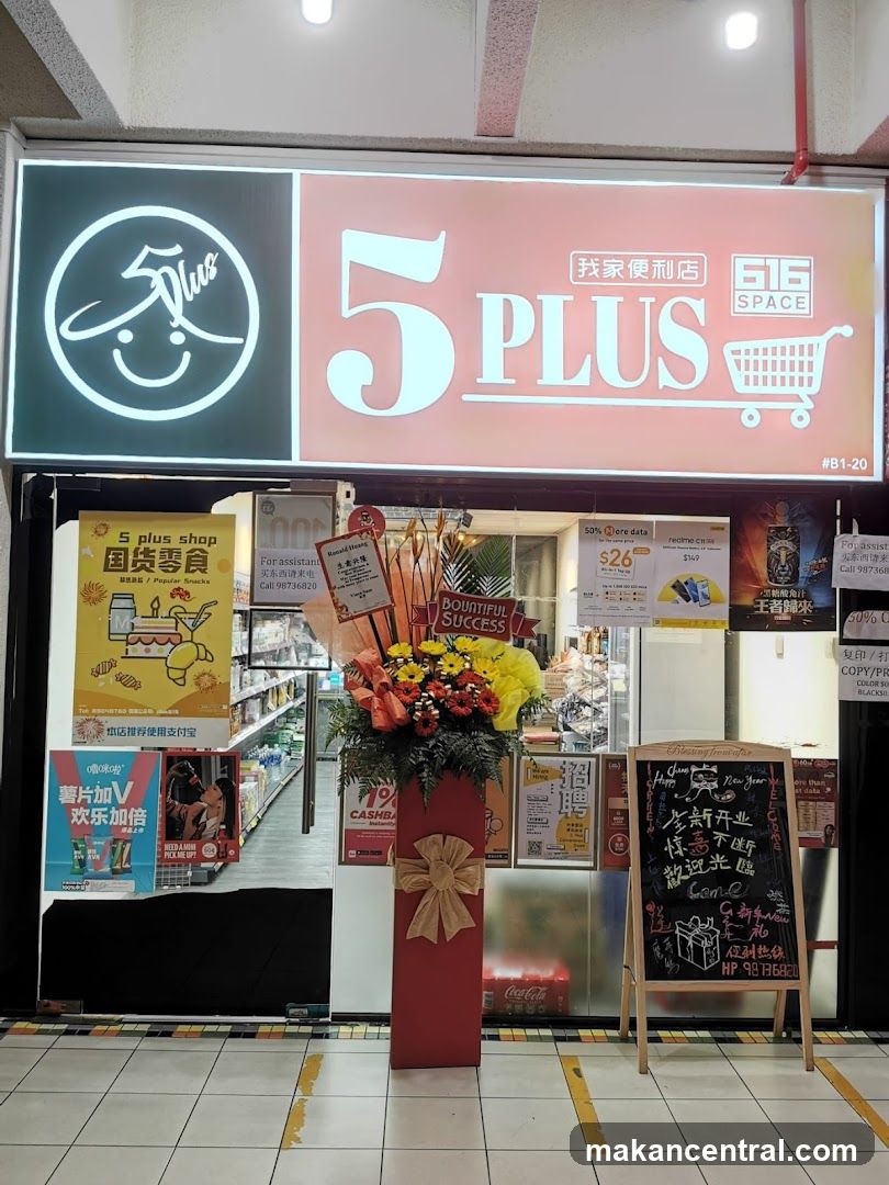 Storefront with illuminated sign featuring '5PLUS' logo, shopping cart icon, and Chinese characters '我家便利店'. A red floral arrangement stands in front of the entrance. To the right is a chalkboard stand advertising New Year promotions. The interior shows shelves stocked with products and promotional posters on display windows.