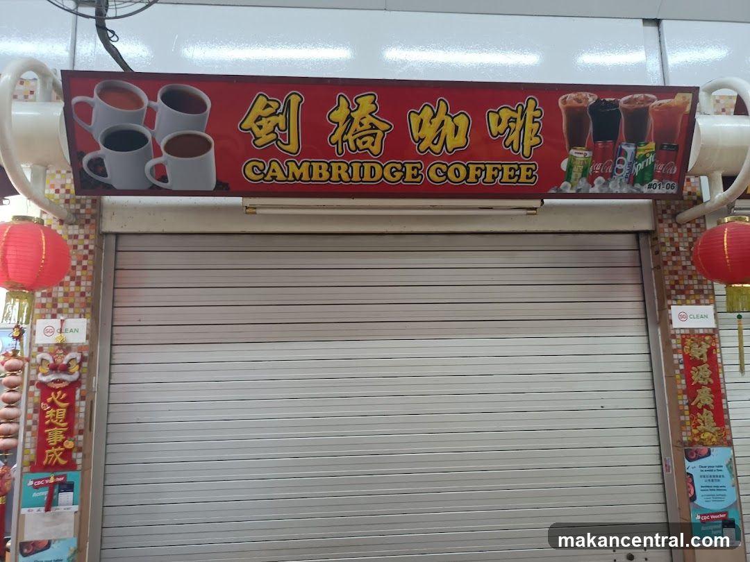 Closed storefront with metal roller shutter door. Above the entrance is a red signboard featuring Chinese characters "剑桥咖啡" (Cambridge Coffee) in yellow font, alongside images of coffee cups and soft drinks like Coca-Cola and Sprite. Red lanterns hang on either side. Vertical red banners with gold Chinese calligraphy flank the shutter. Two 'CLEAN' stickers are affixed to the walls beside the door.
