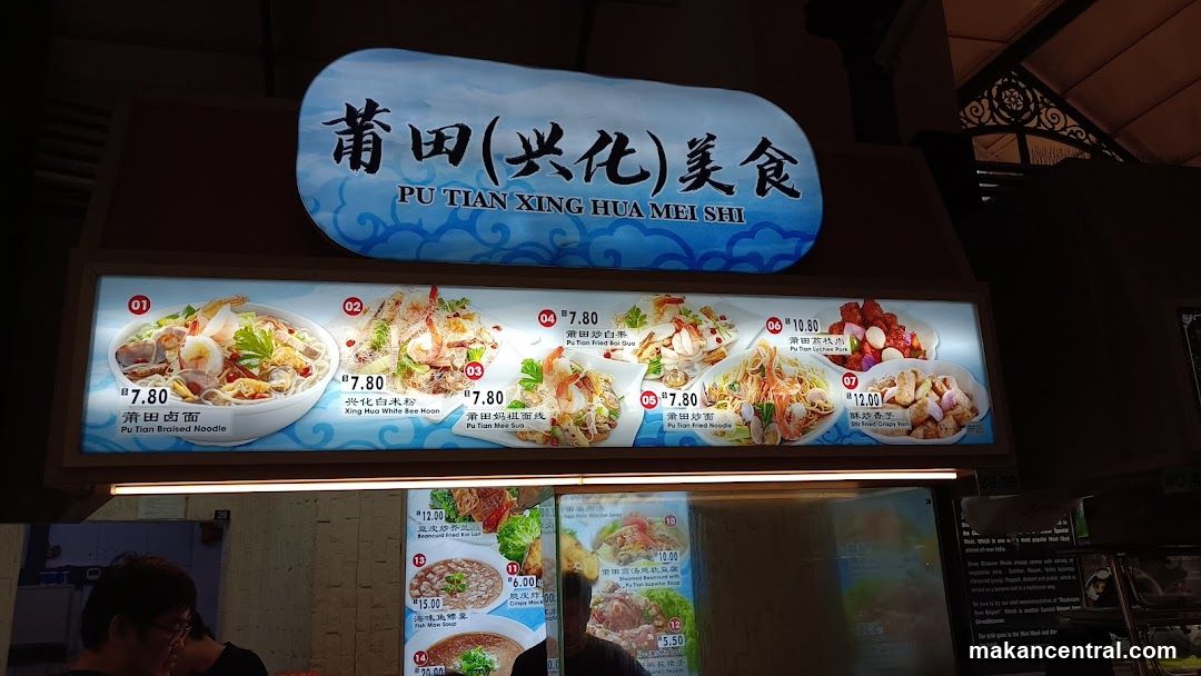 A brightly lit digital menu board displaying seven dishes with prices in Malaysian Ringgit. The sign above reads '莆田(兴化)美食' and 'PU TIAN XING HUA MEI SHI'. Items include Pu Tian Braised Noodle, Xing Hua White Rice Noodles, Pu Tian Fried Koi Suan, etc.