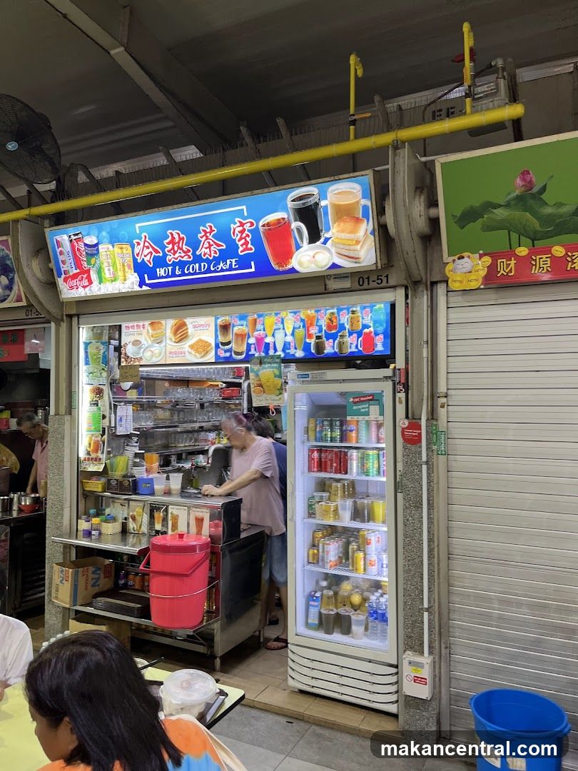 Exterior storefront of a beverage stall with illuminated sign displaying '冷熱茶室' and 'HOT & COLD CAFFE'. A staff member is behind the counter, and a refrigerated display unit filled with drinks and canned beverages stands beside the shop. The entrance has a yellow pipe overhead and adjacent shuttered door with Chinese characters.