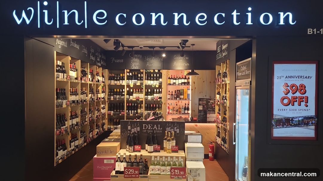 Store entrance with illuminated 'wine connection' sign above the doorway. Interior shows wine racks, promotional displays, and a glass door to the right. A poster on the wall advertises a 25th anniversary sale.