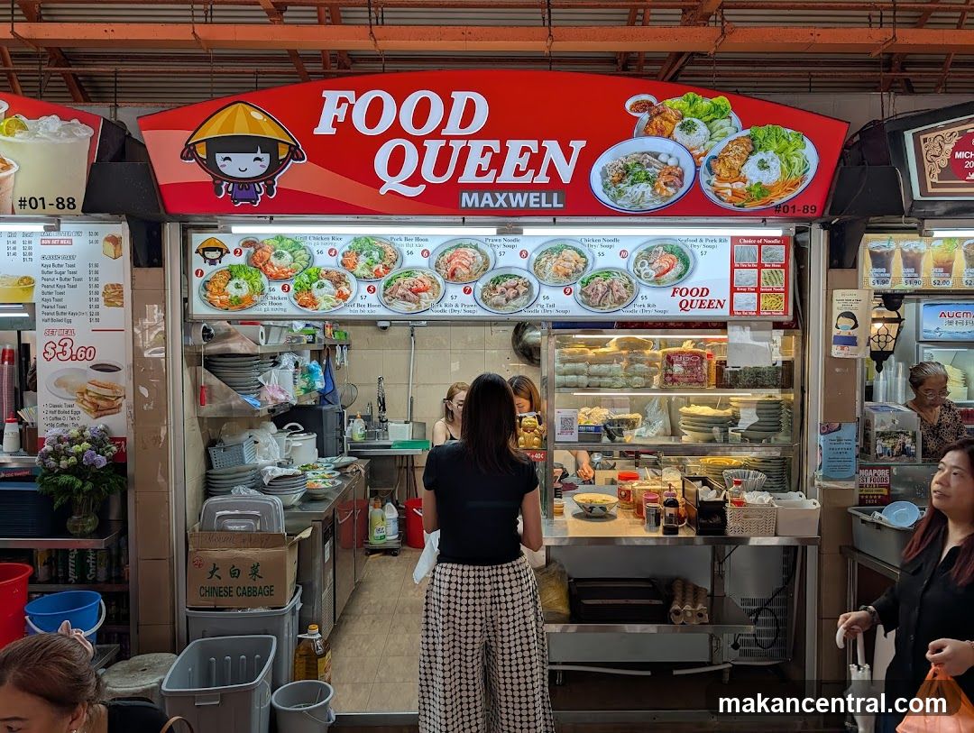 Red signboard with cartoon character and 'FOOD QUEEN MAXWELL' text above a food stall entrance. Visible interior includes counter, display shelves, staff, and customers. Signage is mounted on the physical storefront facade.