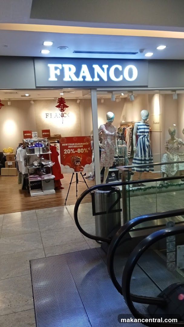 Store entrance with illuminated "FRANCO" sign above glass facade. Inside, mannequins display clothing, including a floral dress and striped dress. A red promotional banner reads "NEW YEAR CLEARANCE NOT SELLING 20%-80%". A tripod stands near the display. An escalator is visible in foreground.