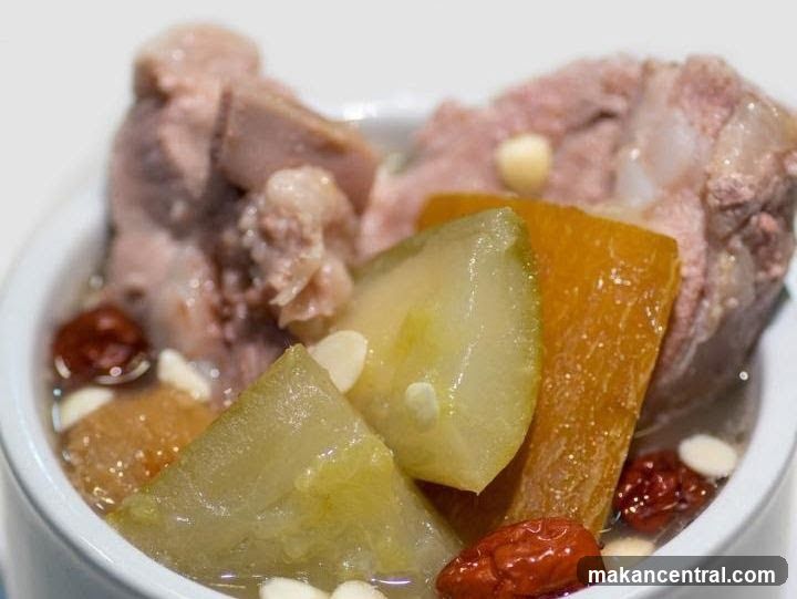 Close-up of a bowl containing cooked meat, sliced vegetables, red dates, and nuts submerged in broth.