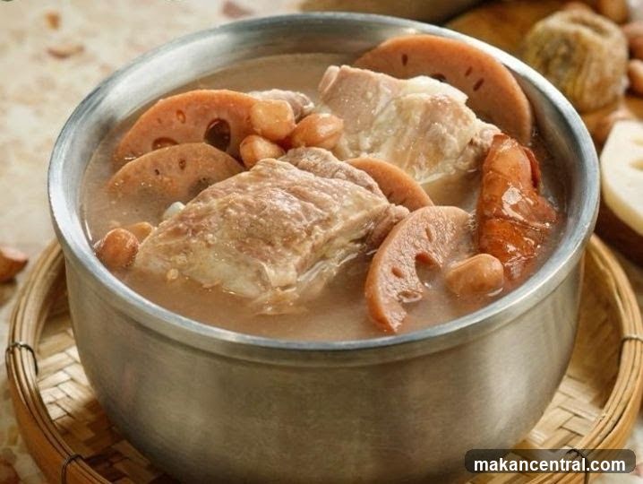 A metal bowl filled with a hearty soup containing chunks of meat, lotus root slices, and peanuts, resting on a woven bamboo tray. The background shows blurred ingredients like dried fruits or nuts. The focus is on the food presentation in a warm, rustic setting.