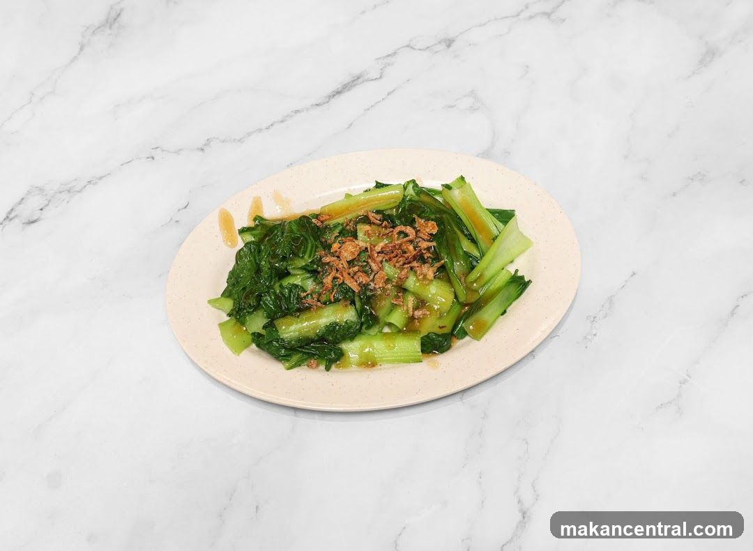 A plate of stir-fried green vegetables topped with crispy fried ingredients, served on a light-colored oval plate placed on a white marble surface.