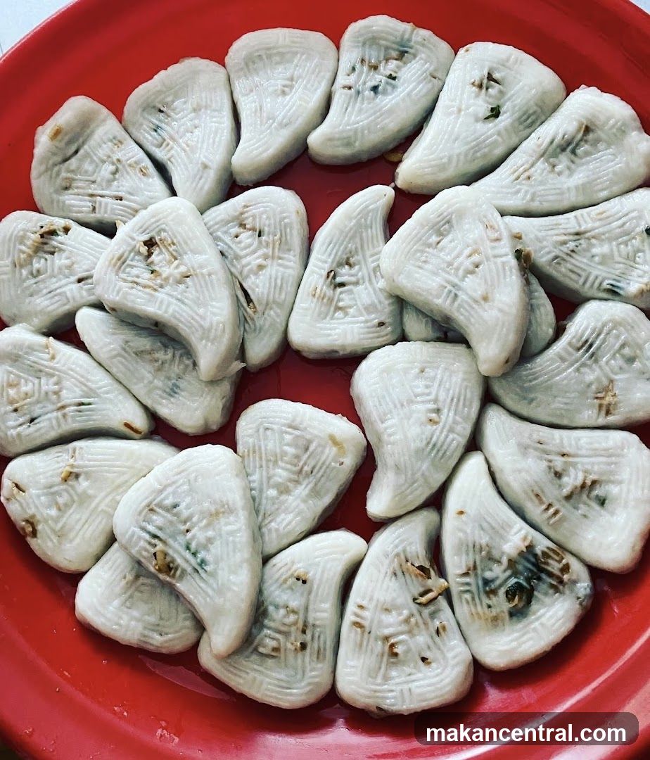 A red plate holds numerous white, crescent-shaped dumplings with embossed patterns and flecks of green and brown ingredients. The food is arranged in a circular pattern.