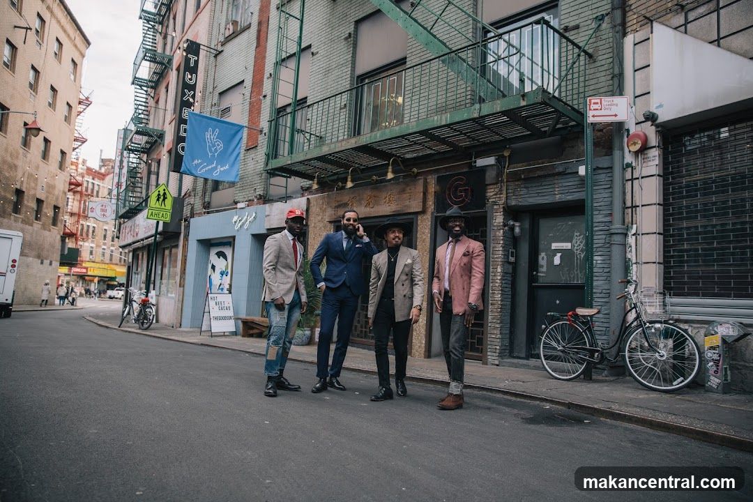 Four men in stylish suits stand on a street in front of businesses.