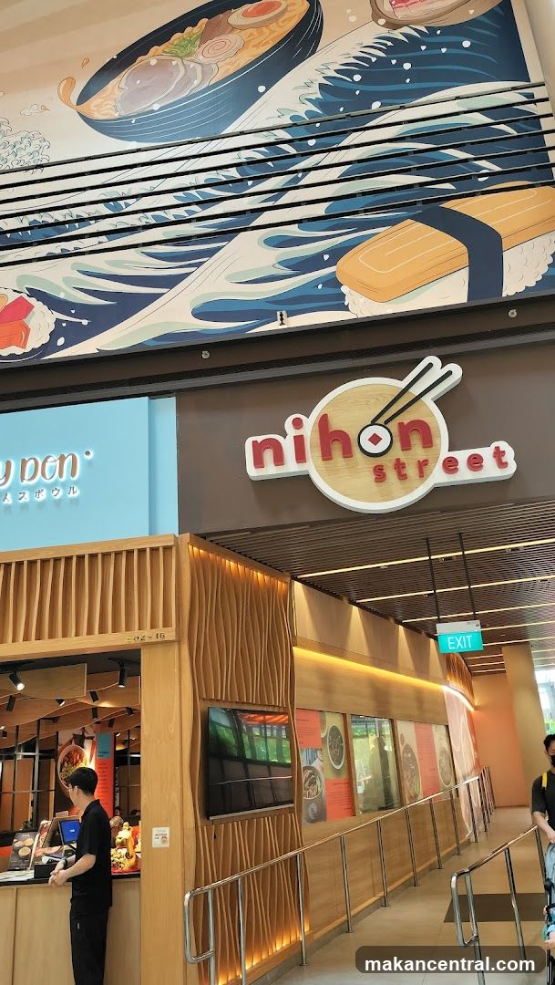 The exterior of a Japanese restaurant called Nihon Street. A large mural above the entrance depicts a bowl of ramen and sushi with waves. The restaurant has a modern wooden facade with a prominent sign. An exit sign is visible.