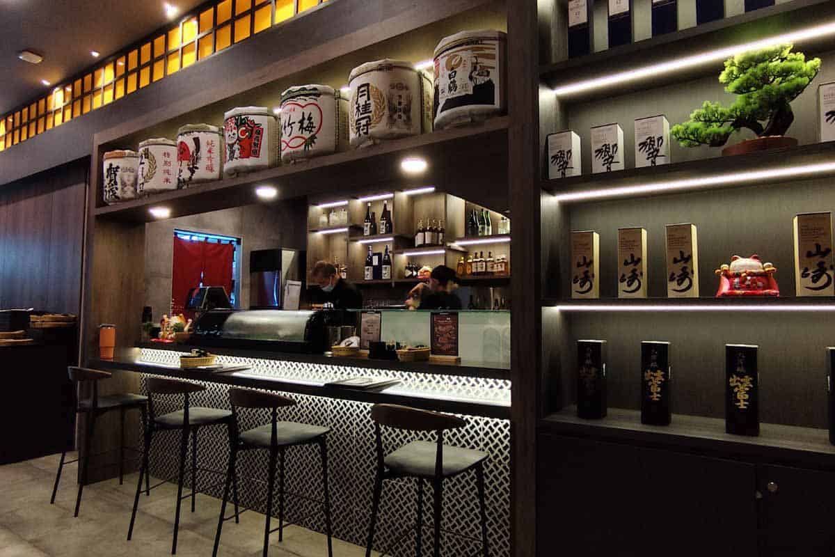 Sake bottles and Japanese whisky lined up on the bar at Kokoro Izakaya Lau Pa Sat, ready for the after-work izakaya crowd